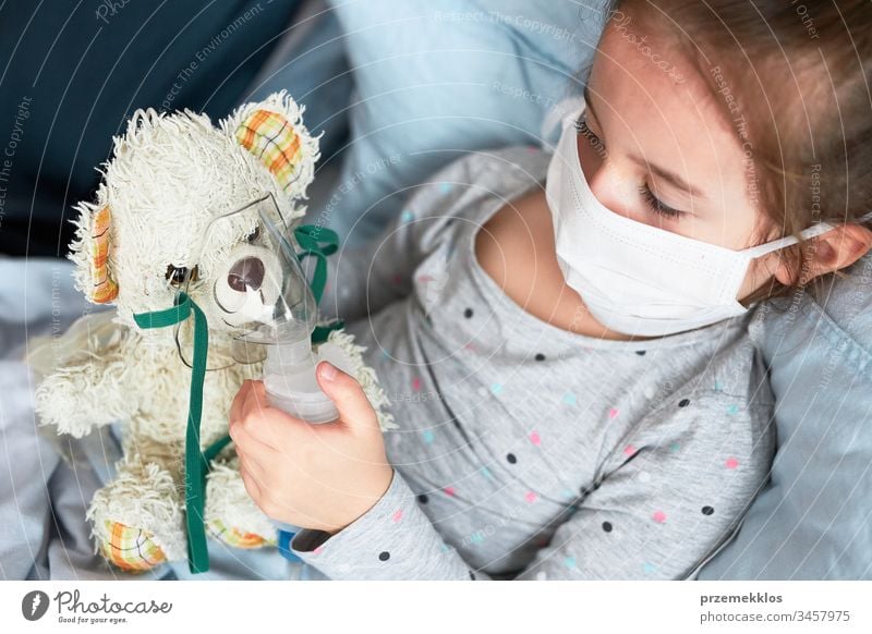 Sick child recovering in bed. Little girl playing by applying medical inhalation treatment with nebuliser to her teddy bear virus infection doctor flu ill sick