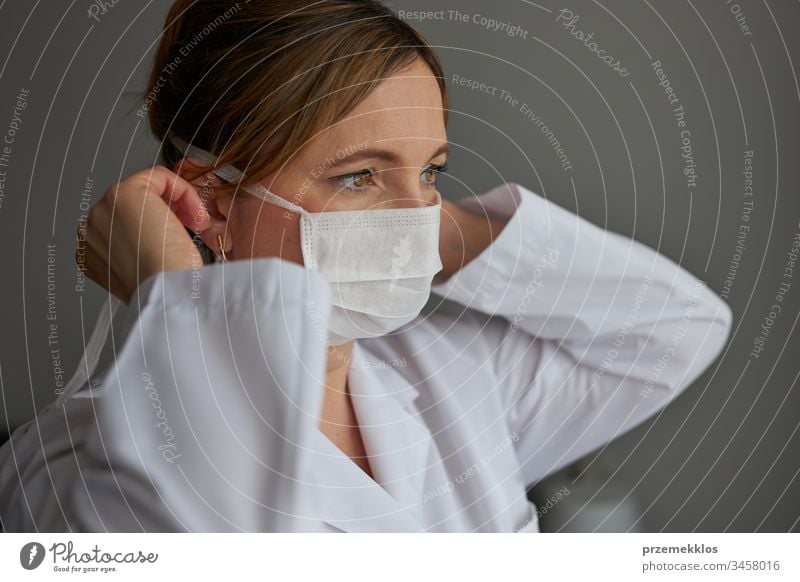 Doctor covering her face with mask. Portrait of young woman wearing the uniform and mask to avoid virus infection and to prevent the spread of disease. Real people, authentic situations