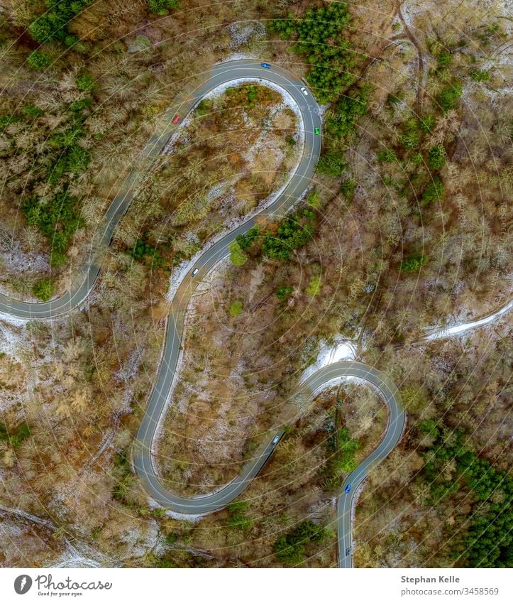 A winding road taken with a drone from above with moving cars in winter with partially lying snow. Street Aerial photograph Exterior shot Day