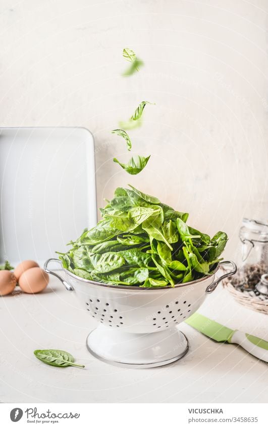 Colander with spinach and falling spinach leaves on white kitchen table. Healthy food concept colander healthy food delicious bowl bunch nutrition cooking diet