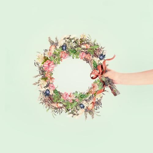 Female women hand holding summer flowers wreath with ribbon at light mint background. Creative flowers arrangement concept female creative anniversary art