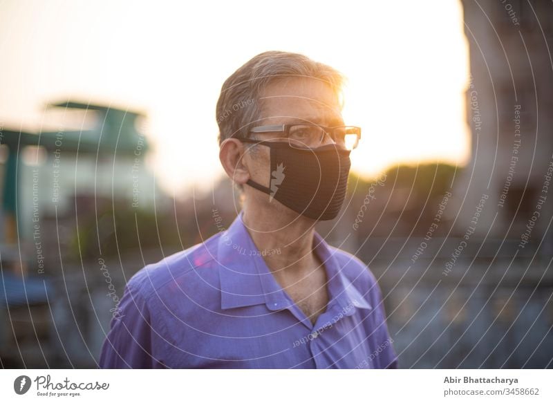 Close up portrait of an Indian old man with corona preventive mask on a rooftop during sunset in home isolation.Indian lifestyle, disease and home quarantine.