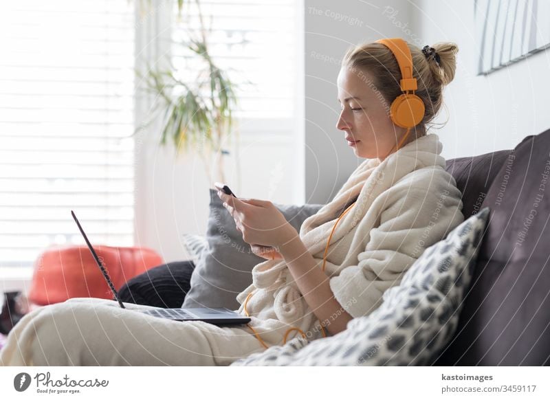 Social distancing. Stay at home. Woman in bathrobe being comfortable at her home sofa, using social media apps on phone for video chatting and stying connected with her loved ones.