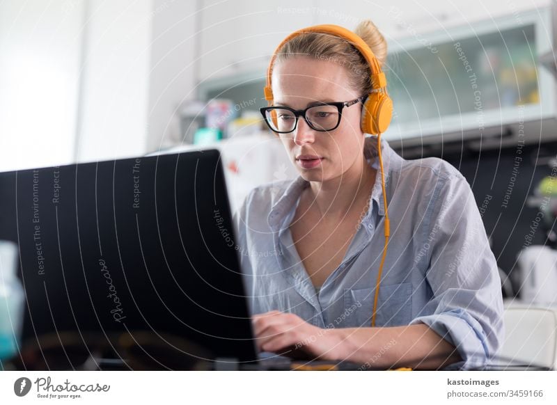 Female freelancer in her casual home clothing working remotly from her dining table in the morning. Home kitchen in the background. Socaila distancing. Stay at home.