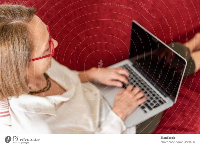 Elegant mature woman using computer at home elderly lady aged beauty wellbeing carefree comfort attractive comfortable casual blond relaxed middle-aged leisure