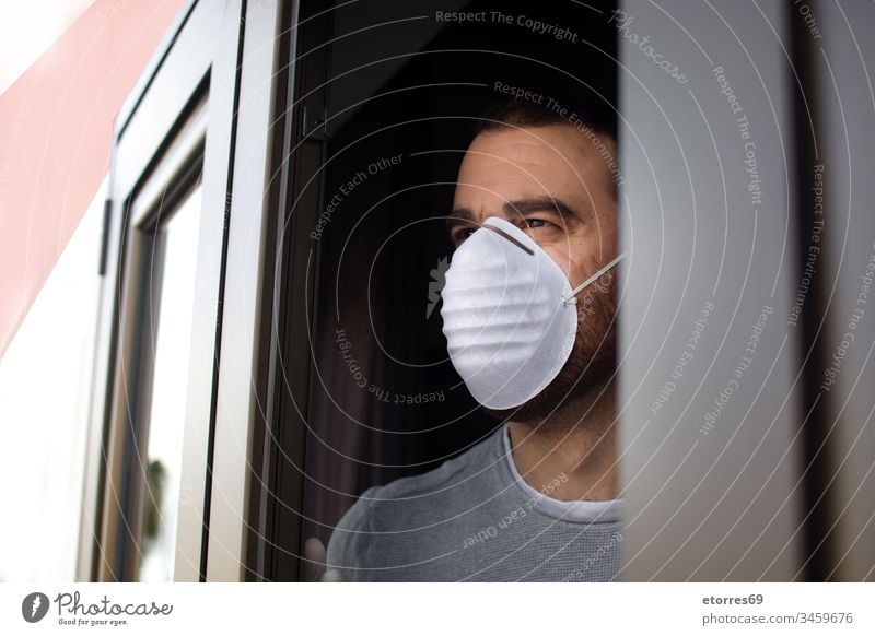 Man with face mask and gloves looking out the window man coronavirus quarantine covid-19 confinement disposable stay at home care caucasian concept health house