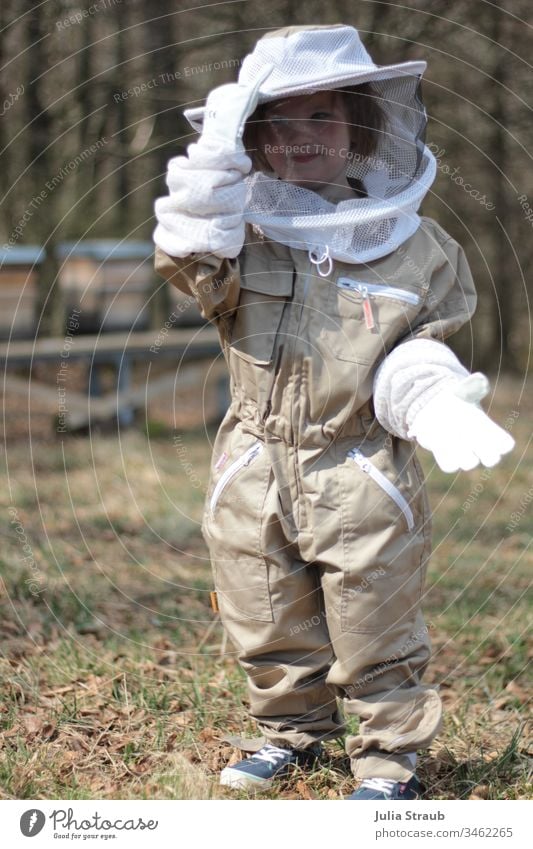 Little child in a beekeeper protection suit with gloves keep beekeepers Suit Protective clothing Gloves Hat Pride Sweet Beehive Prey Forest Nature Clearing Girl
