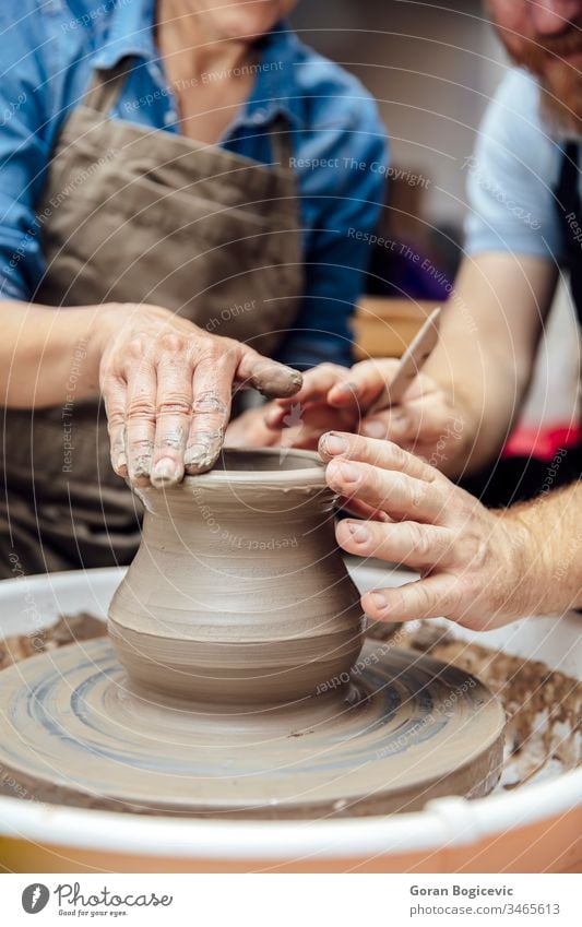 Senior woman spinning clay on a wheel with teacher at pottery class lady instruction instructor learn shape finger turn ceramic skillful artist shaping hand