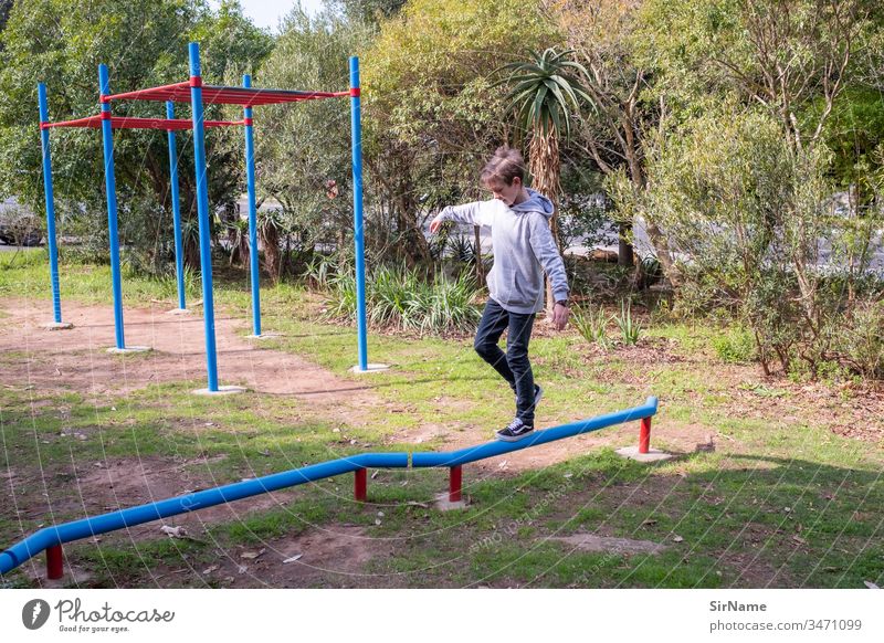 Boy (child) balancing on a low bar at a playground Playground sunny outdoors shrubs Grass