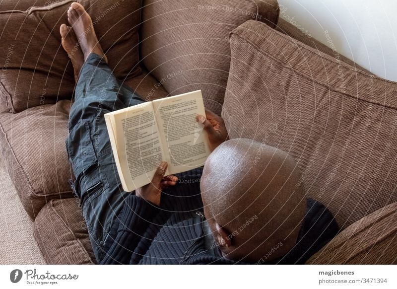 Black man, of African ethnicity, reading on the sofa 40s Caribbean adult african american black book british casual comfort comfortable concept couch down