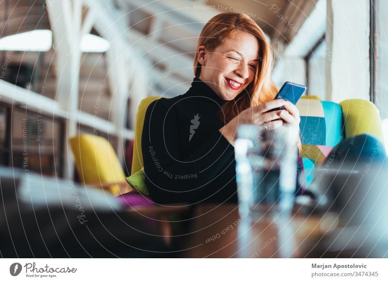 Young happy woman using smartphone in a cafe young smile indoor casual smiling table sitting lifestyle connected connection mobile massaging communication