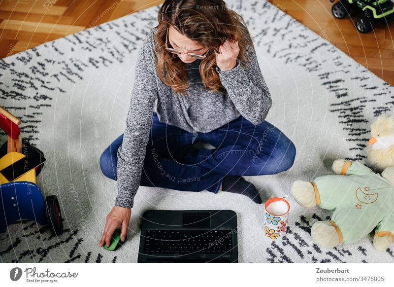 Woman sitting cross-legged in the children's room with toys and working on the laptop home office Toys Children's room Sit Cross Legged labour Stayhome Carpet