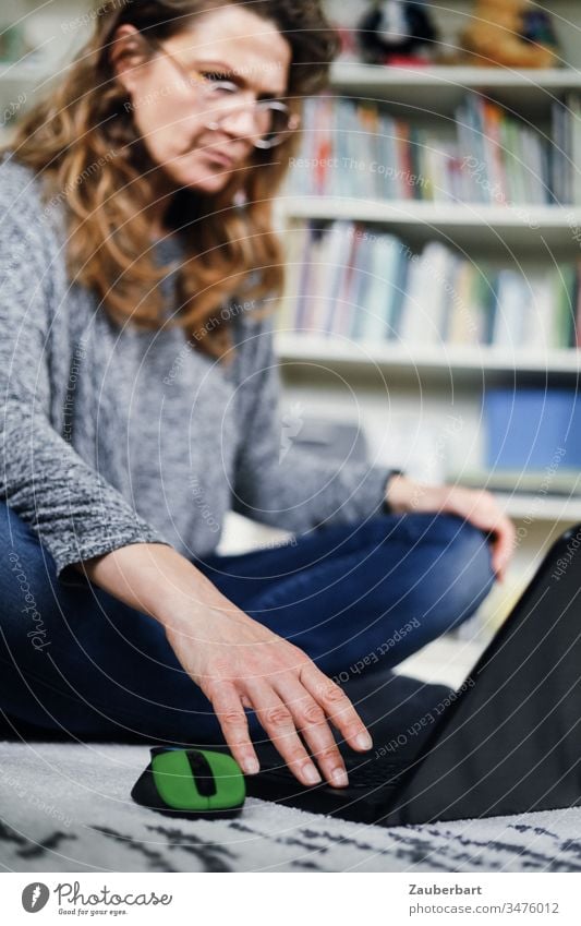Woman sits on the floor of her home office and looks at her laptop with concentration concentrated Exasperated Reading Ground Carpet Computer Notebook Mouse