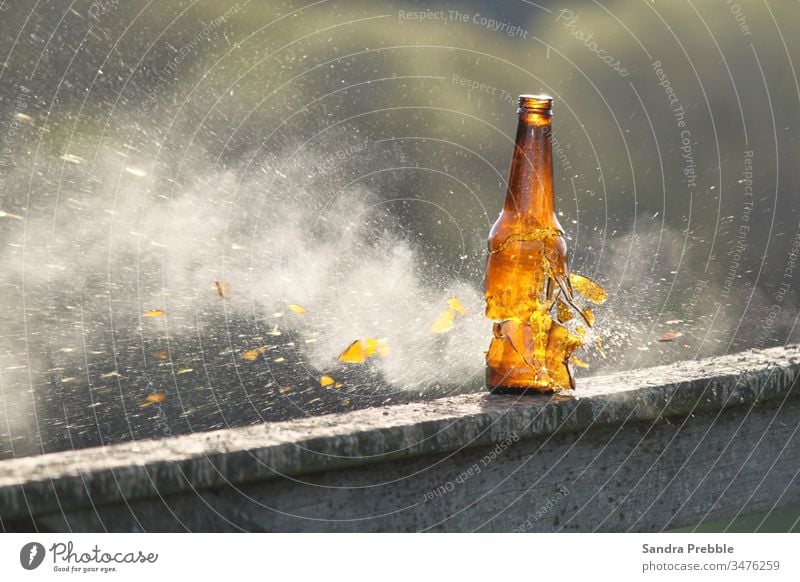 A beer bottle is shot and the pieces of glass begin to shatter as the smoke drifts brown bottle frozen action glass shatters target practice drinking games
