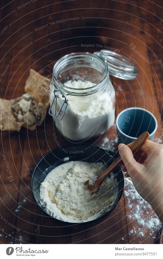 A woman's hand mixing sourdough with a wooden spoon. Bakery concept. Sourdough Dough knead flour yeast processing glass jar homemade wooden bottom