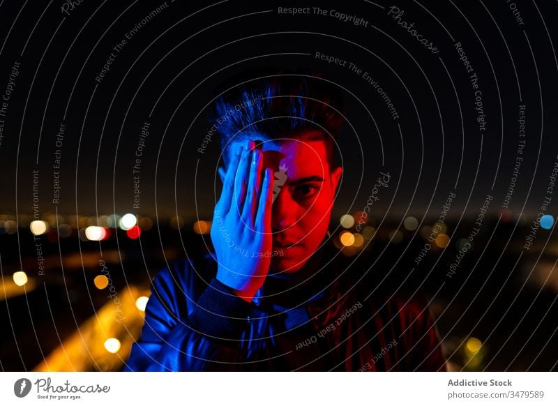 Modern man covering face under colorful illumination cover face half night illuminate concept street city urban dark male gesture young modern casual town