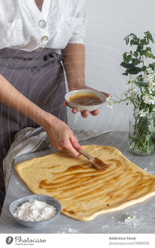 Crop woman spearing apple sauce on dough smear puree pastry cook table flour flower female bouquet apron kitchen prepare food ingredient cuisine recipe chef