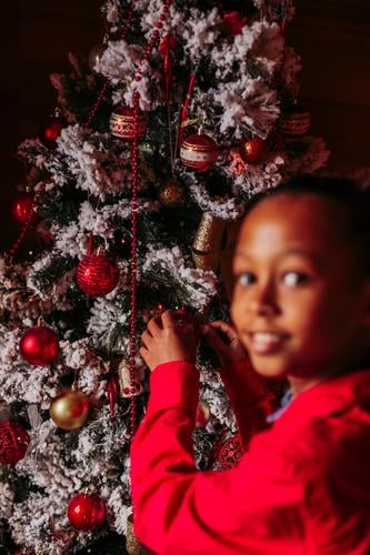 Happy little girl decorating Christmas tree kid christmas decorate tradition home rustic ethnic smile happy casual cheerful positive female enjoy festive black