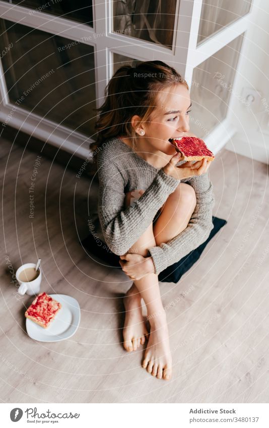 Young woman sitting on floor and eating breakfast toasts home coffee positive casual enjoy morning sweet smile relax content alone happy young female lifestyle