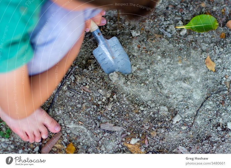 Barefoot child digging in dirt with shovel children kids boy son playing outside garden gardening exterior shot playing in dirt people joy backyard young