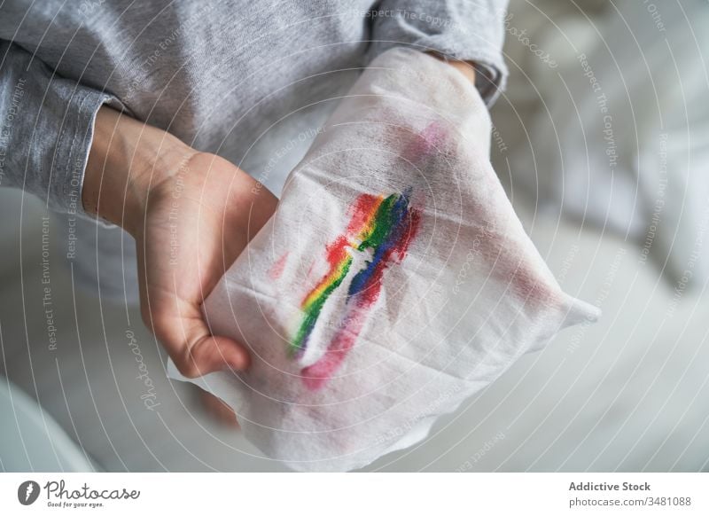 Anonymous child holding wipe while removing rainbow make up home quarantine concept napkin show symbol smile kid pandemic epidemic remove isolation paint