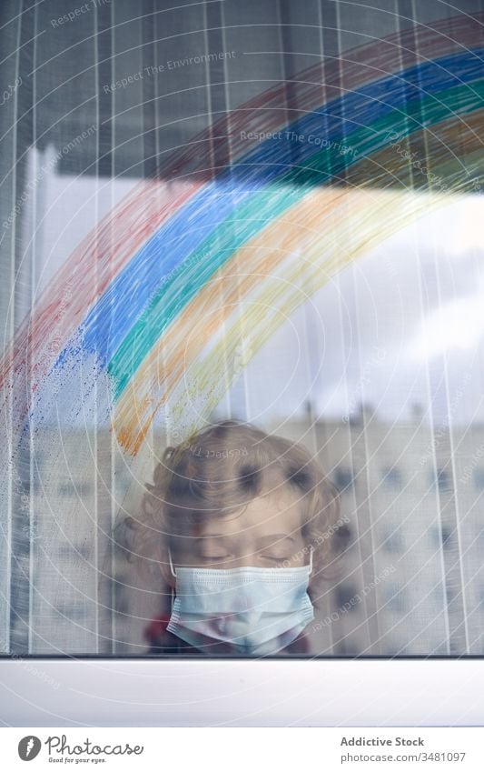 Boy behind window during quarantine boy mask medical rainbow colorful home hospital frown pandemic coronavirus covid 19 child kid childhood sad unhappy hygiene