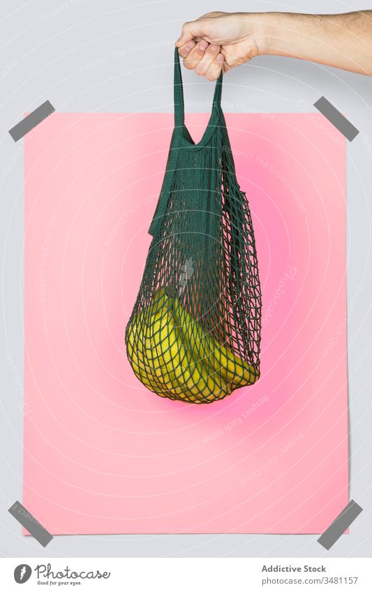 Crop person carrying string bag with bananas zero waste grocery concept eco friendly rectangle bright colorful organic shop pink package net vivid sack vegan