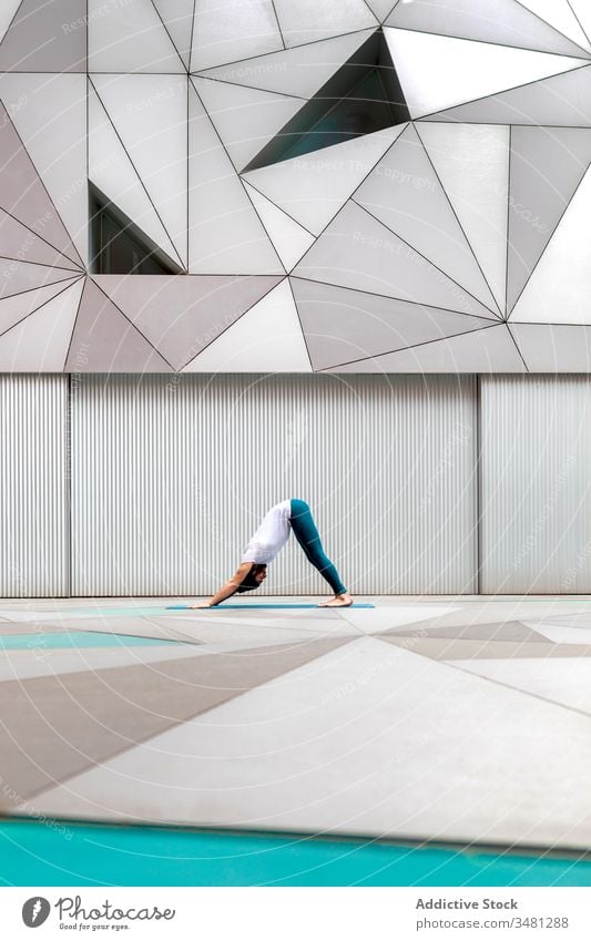 Man doing yoga in spacious room man exercise training geometry downward facing dog pose modern stretch fitness shape male sportswear architecture contemporary