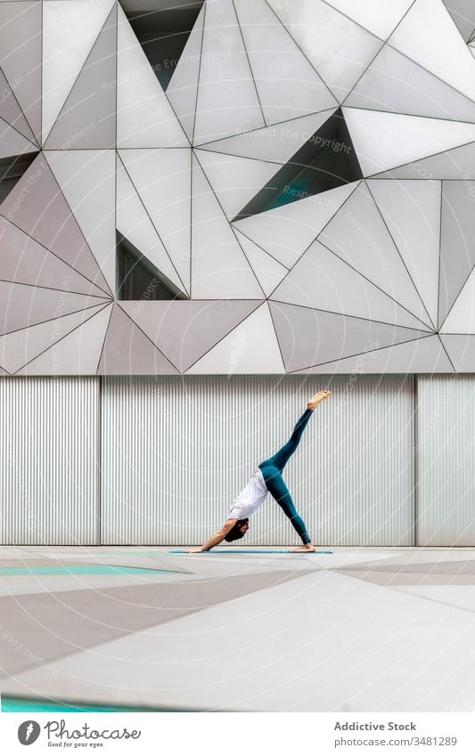 Slim guy performing yoga exercise in geometric room man training geometry modern stretch fitness shape male sportswear architecture contemporary wall spacious