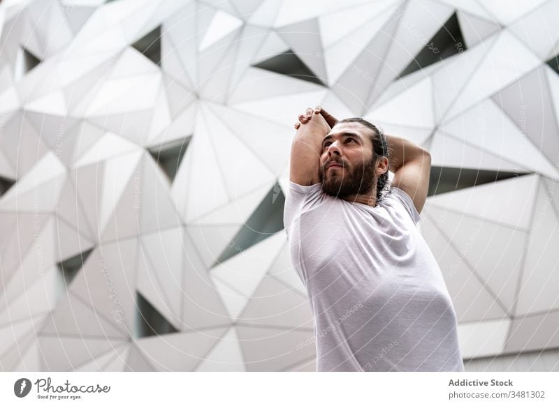Bearded man stretching arms during yoga training exercise geometry modern fitness shape wall male sportswear architecture contemporary zen flexible workout