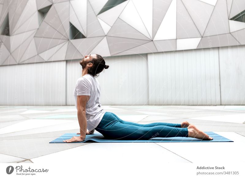 Adult man stretching back on mat yoga exercise training geometry upward facing dog pose modern fitness shape male sportswear architecture contemporary wall