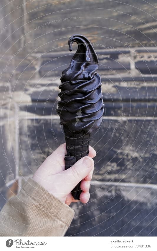 hand holding black soft serve ice cream cone made with activated charcoal icecream food trend creemee carbon trendy ice-cream waffle dessert sweet cold summer
