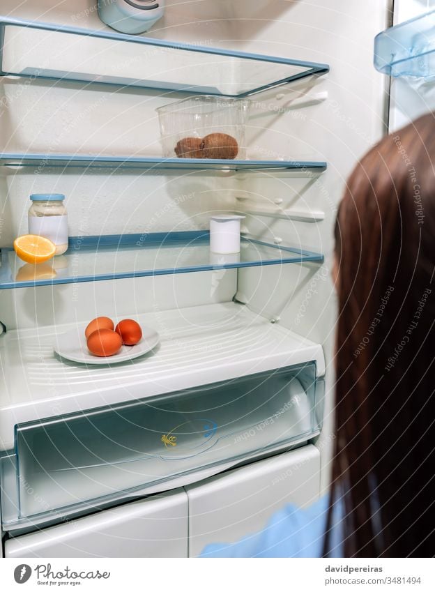 Girl looking at empty fridge due to a crisis unrecognizable girl covid-19 economic problems coronavirus hungry poverty no food kitchen people refrigerator home
