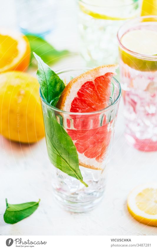 Summer refreshing drink with grapefruit slices and green leaves in sunlight on white table , close up. Infused detox  water. Vitamin C. Antioxidant summer