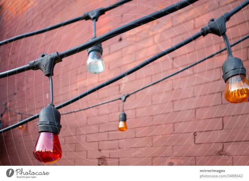 Lighting decorations of colored big light bulbs hanging down from thick black electrical wire outside outdoors brick wall lighting equipment lamp decorative