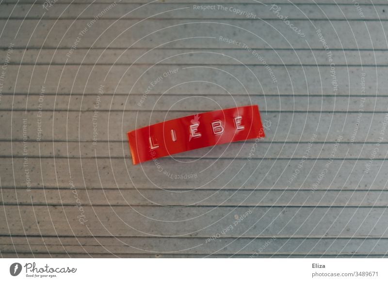 A red label with the word love written on it Love Label Word authored Letters (alphabet) Characters Deserted Gray writing Text Emotions Neutral Background Metal