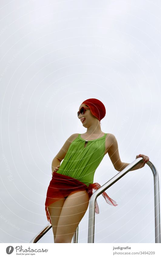 The girl with the beautiful red bathing cap and green swimsuit is standing at the edge of the pool with red sunglasses. A summer love. Girl Woman Swimwear