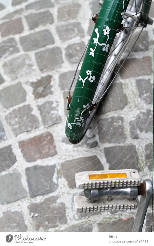 Green fender from a bicycle, painted with flowers in hippie look, on cobblestone on a path, opposite a bicycle pedal with reflector. Bicycle Wheel Guard Tin