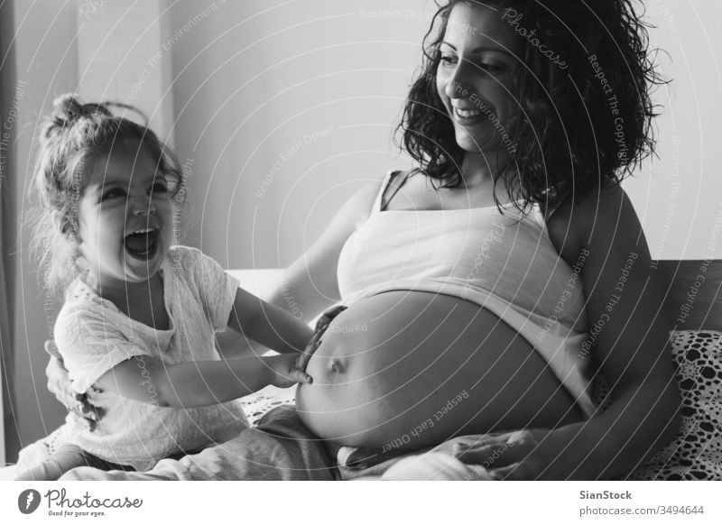 Happy kid girl with her pregnant mother on the bed child woman pregnancy mom belly family white baby happy little love lying young bedroom maternity beautiful