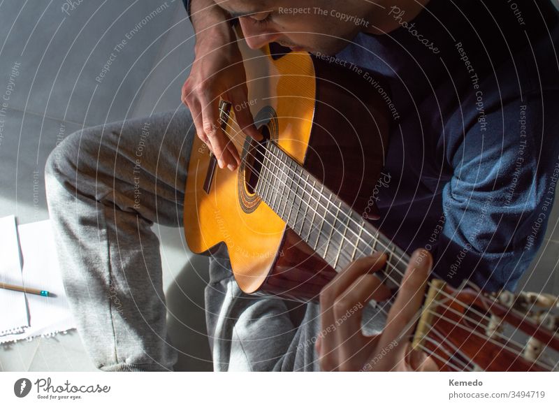 Top view of a young man playing guitar and composing music at home. Casual man sitting on the floor learning guitar. guitarist write practice casual top above