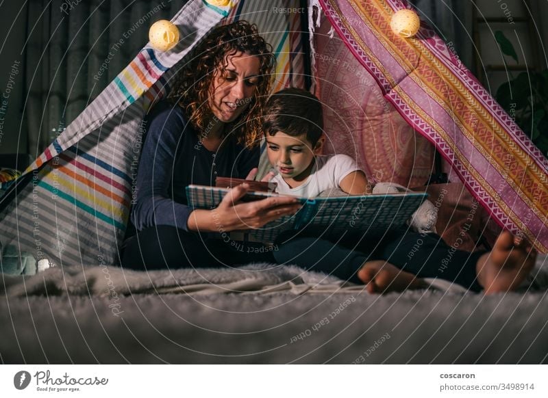 Mother and son reading a book on a tent at home beautiful bedroom bedtime caucasian child childhood concept cute dark daughter day education family female