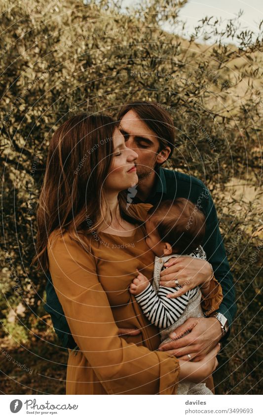 Couple standing with their son outdoors. Young family concept. Mother holds the baby in the arms. Man kiss the woman in the cheek. happy park people young