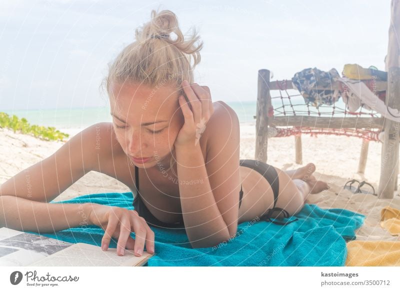 Beautiful girl lying at the beach in her swimsuit and reading a book sand sea summer bikini towel vacation woman beautiful female sexy sunbathing tan travel
