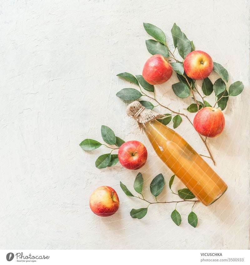 Homemade apple cider vinegar or juice in glass bottle with ingredients: fresh organic garden apples with bunches and leaves on white table background. Top view. Flat lay. Border. Frame. Copy space