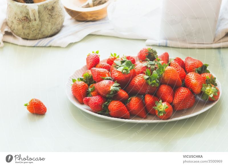 Organic garden strawberries in white plate on light kitchen table . Healthy seasonal food. Ripe berries heap organic healthy ripe above background berry bowl