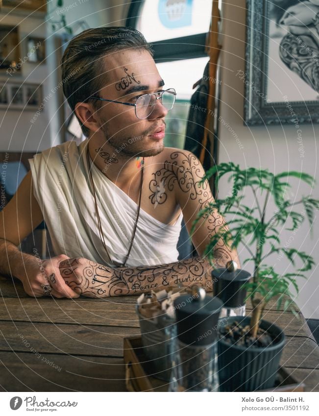 Young bearded man in toga with glasses tattooed with UN SDG tattooes Ornament Ornamental united nations sdg sdgs peace and justice goal 8 16 unusual Café coffe