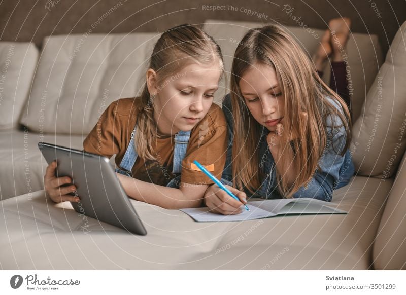 Two beautiful sisters do their homework during quarantine. Children use gadgets for learning. Education, distance learning, home schooling during quarantine
