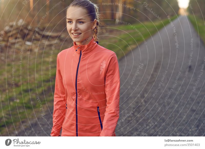 Smiling athletic fit young woman working out on a tarred lane through forests backlit by the warm glow of the sun in a healthy active lifestyle concept face