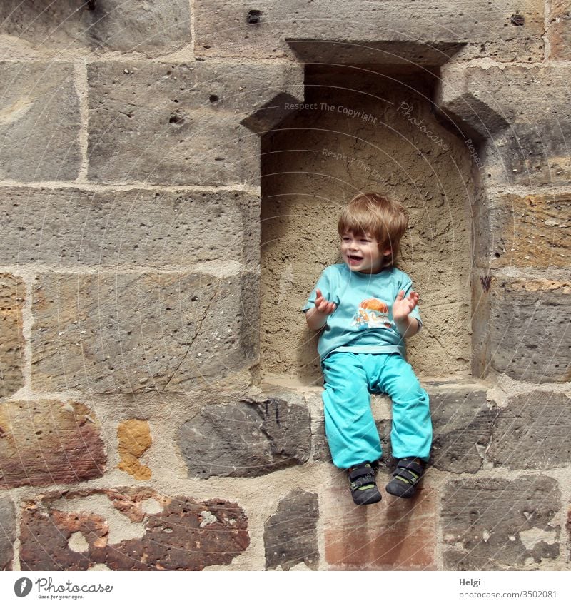laughing little boy sits in a gap in the wall and seems to say " and now...? " Human being Child Toddler Boy (child) masculine portrait youthful Laughter