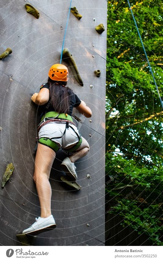 Woman in shorts and black shirt with safety equipment climbing an artifical climbing wall. active activity adult adventure alone beautiful beauty cliff climber